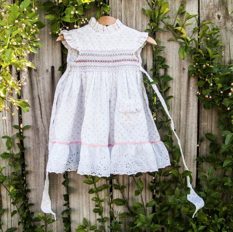 A white child's dress hangs from a wood fence